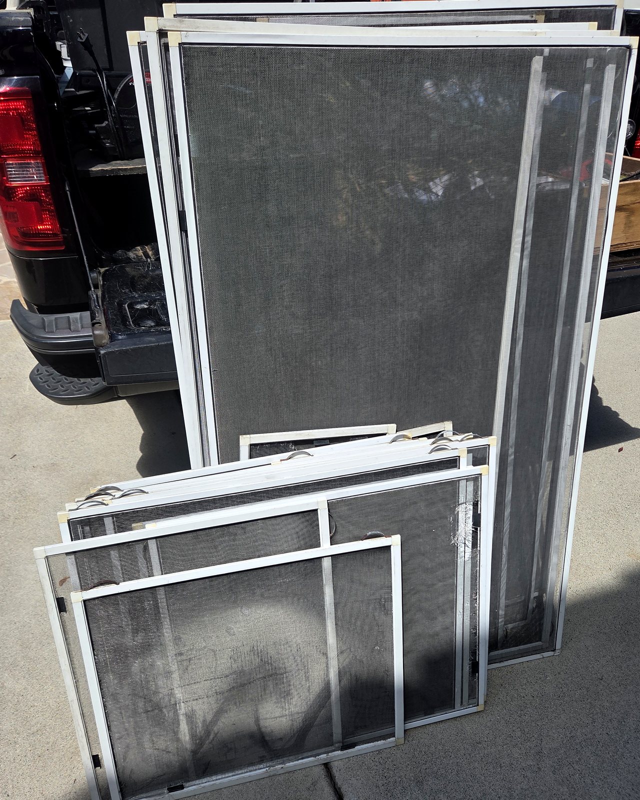 Group of white-framed window screens before repair and rebuilding work