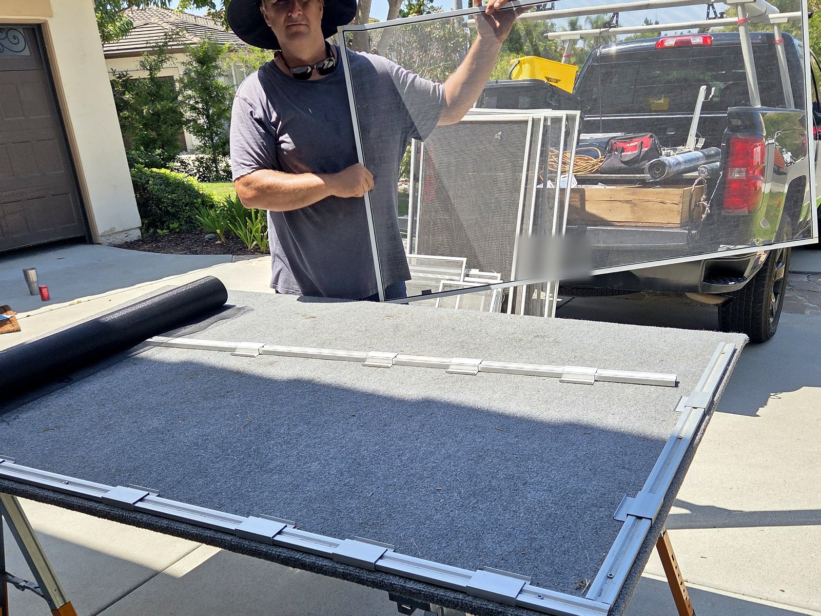 Zac holding a completed white-framed window screen at the mobile worktable